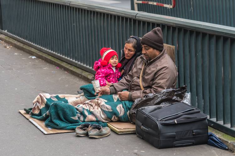 Children sitting on a sidewalk with a parent experiencing homelessness